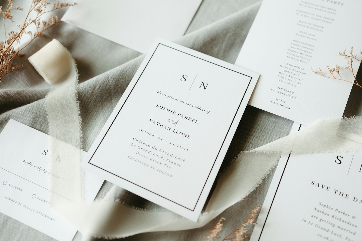 Elegant wedding stationery and dried botanicals on grey fabric.